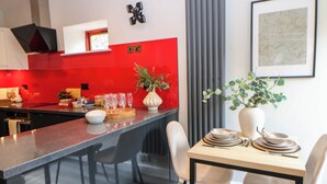 A modern kitchen with a red accent wall, a dining area with a table set for two, and a large window with curtains. - Half Under (Huddersfield)