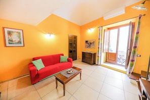 A living room with a red sofa, a wooden coffee table, and a painting on the wall. - Madonie Holidays: Pomelia Apartment (Cefalù)