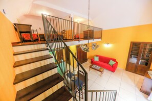 A multi-level living space with a staircase, a red sofa, and a wooden cabinet. - Madonie Holidays: Pomelia Apartment (Cefalù)