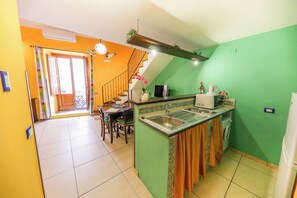 A kitchen with a green wall, a dining area with a table and chairs, and a staircase leading to an upper level. - Madonie Holidays: Pomelia Apartment (Cefalù)