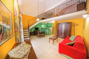 A living room with a red sofa, a dining table with chairs, a staircase leading to an upper level, and a kitchen area with green walls. - Madonie Holidays: Pomelia Apartment (Cefalù)
