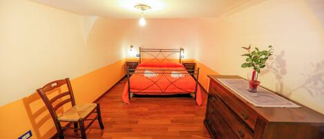 Un dormitorio con una cama, un aparador de madera, una silla y una mesita con una planta.