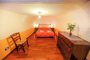 A bedroom with a bed, a wooden dresser, a chair, and a small table with a plant. - Madonie Holidays: Pomelia Apartment (Cefalù)