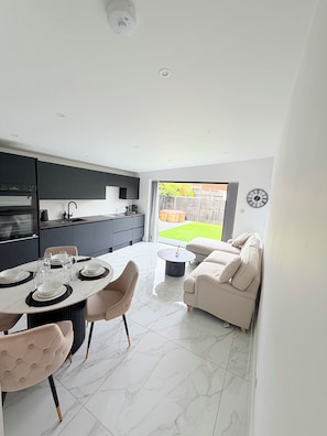 A modern kitchen with dark cabinets, a dining area with a round table and chairs, and a living space with a sofa and a coffee table.