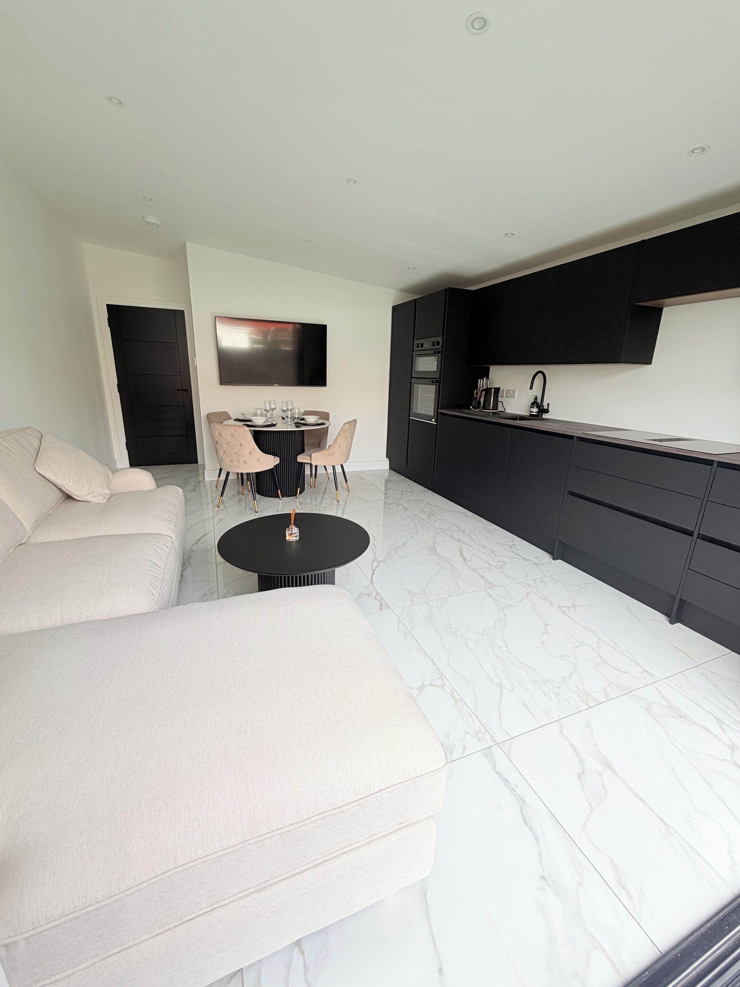 Ein modernes Wohnzimmer mit einer Couch, einem runden Couchtisch und einem Essbereich mit Stühlen und einem Fernseher.