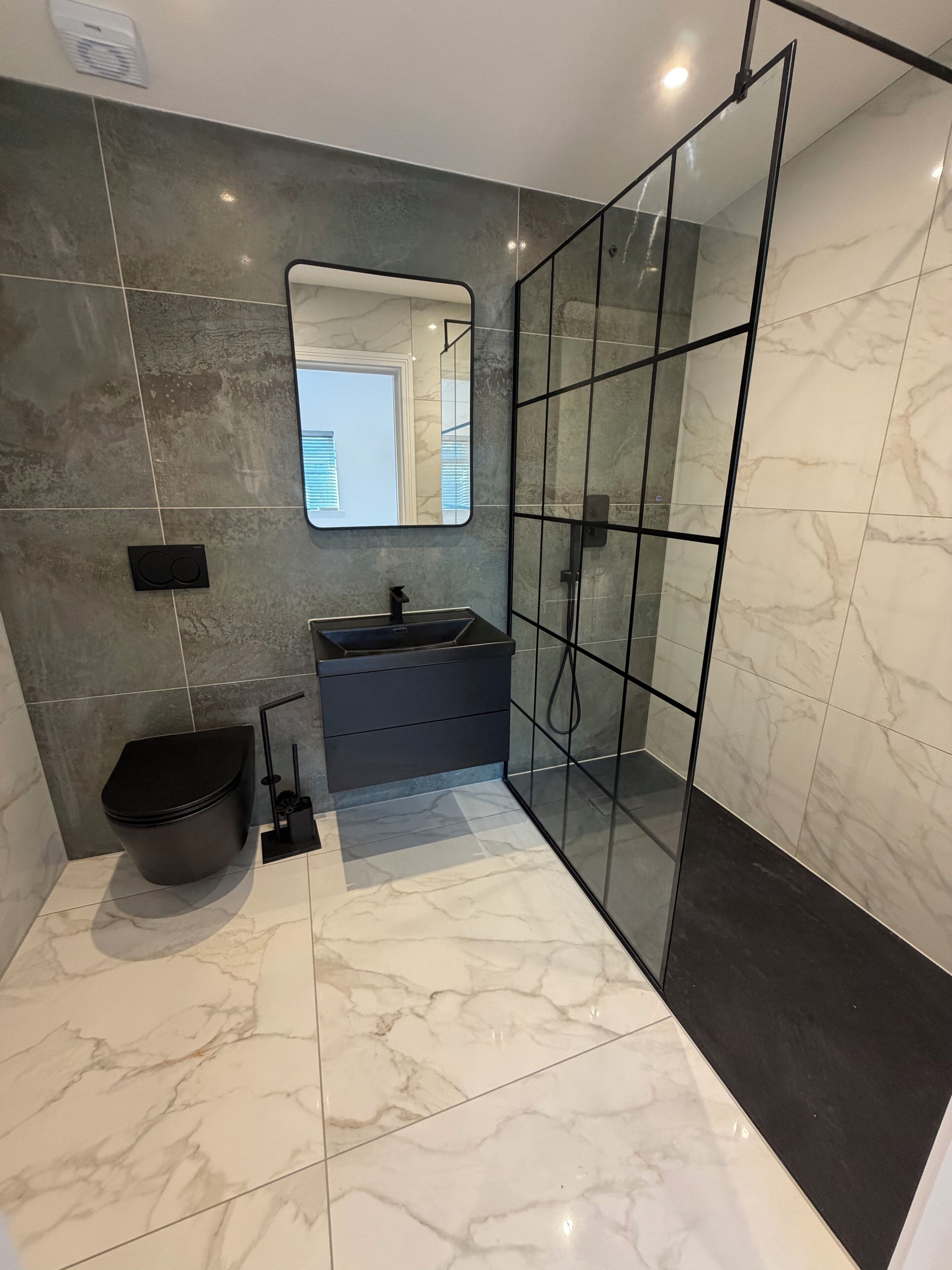 A modern bathroom with a glass shower enclosure, a black toilet, a vanity with a sink, and a mirror.