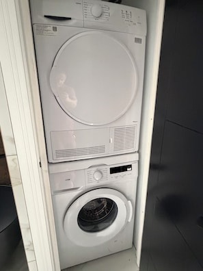 Uma unidade de lavanderia compacta e branca, fixada na parede, com máquina de lavar frontal e secadora.