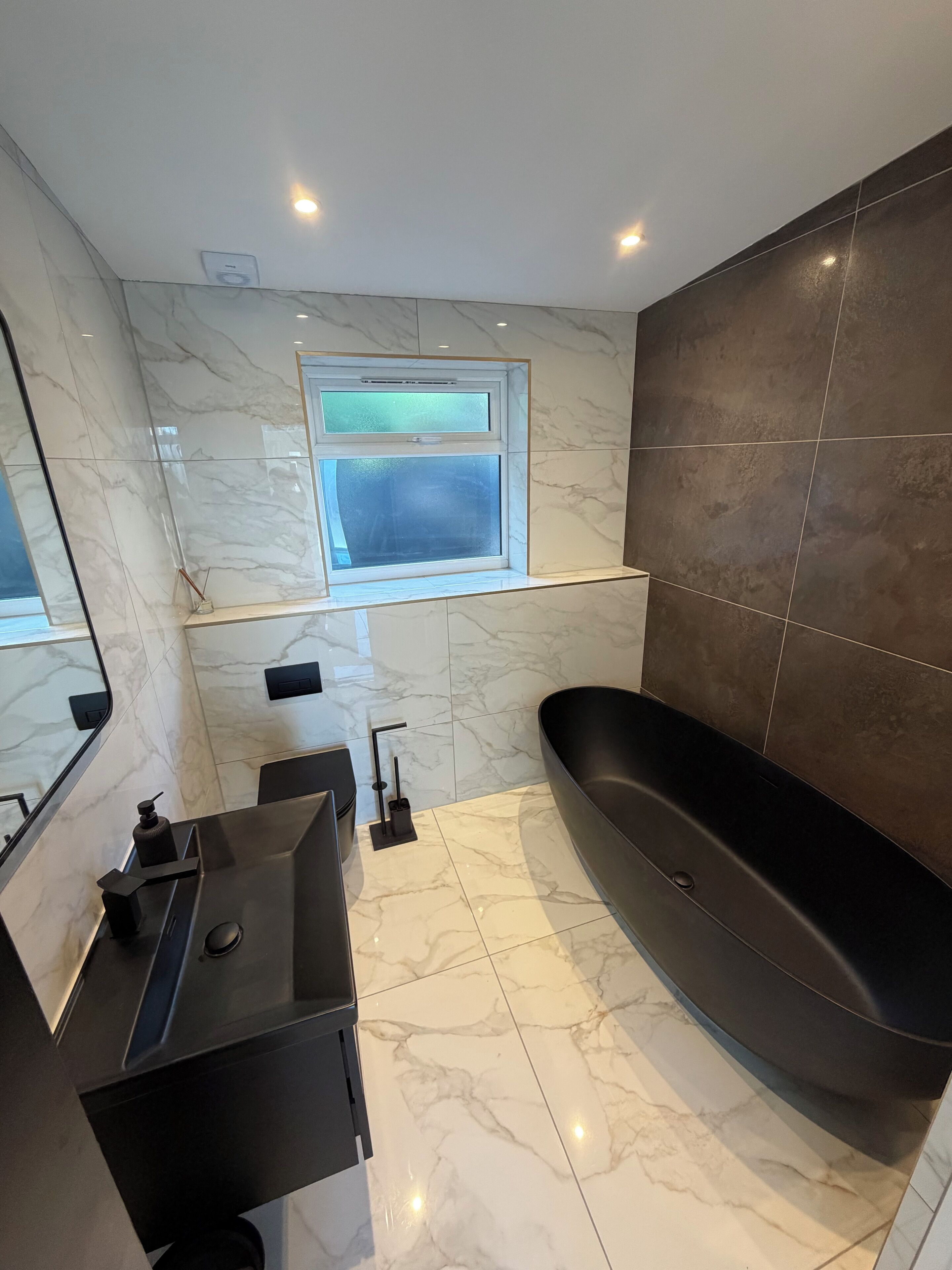 Un baño moderno con una bañera negra, un tocador con espejo y una ventana sobre el lavabo.