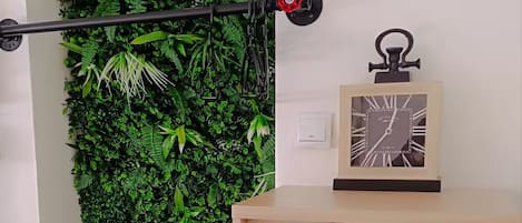 Un mur agrémenté d’un jardin vertical, une tige en métal noir et une horloge posée sur un meuble.