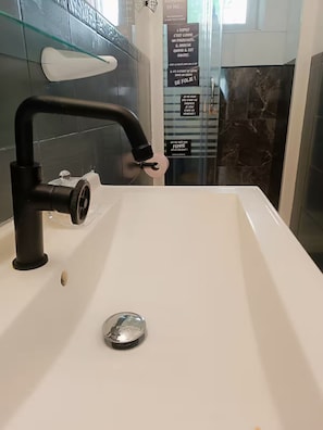 Ett modernt badrum med en vit tvättställ, en svart kran och en duschkabin med glasväggar.