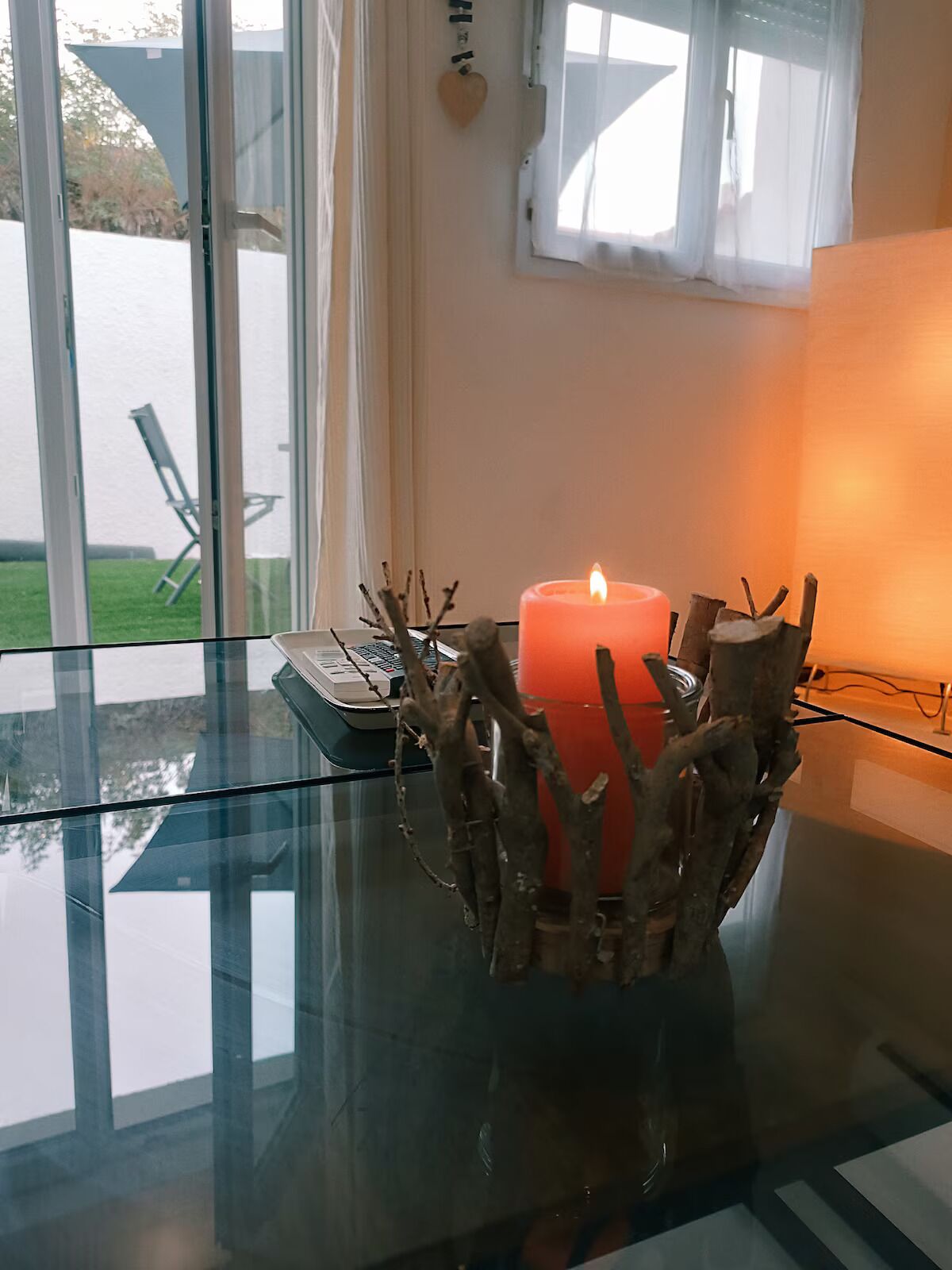 A glass table with a candle in a branch-shaped holder, a keyboard, and a window with a view of a lawn and chairs.