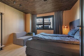 A bedroom with a bed, a sofa, a window, and a lamp.
