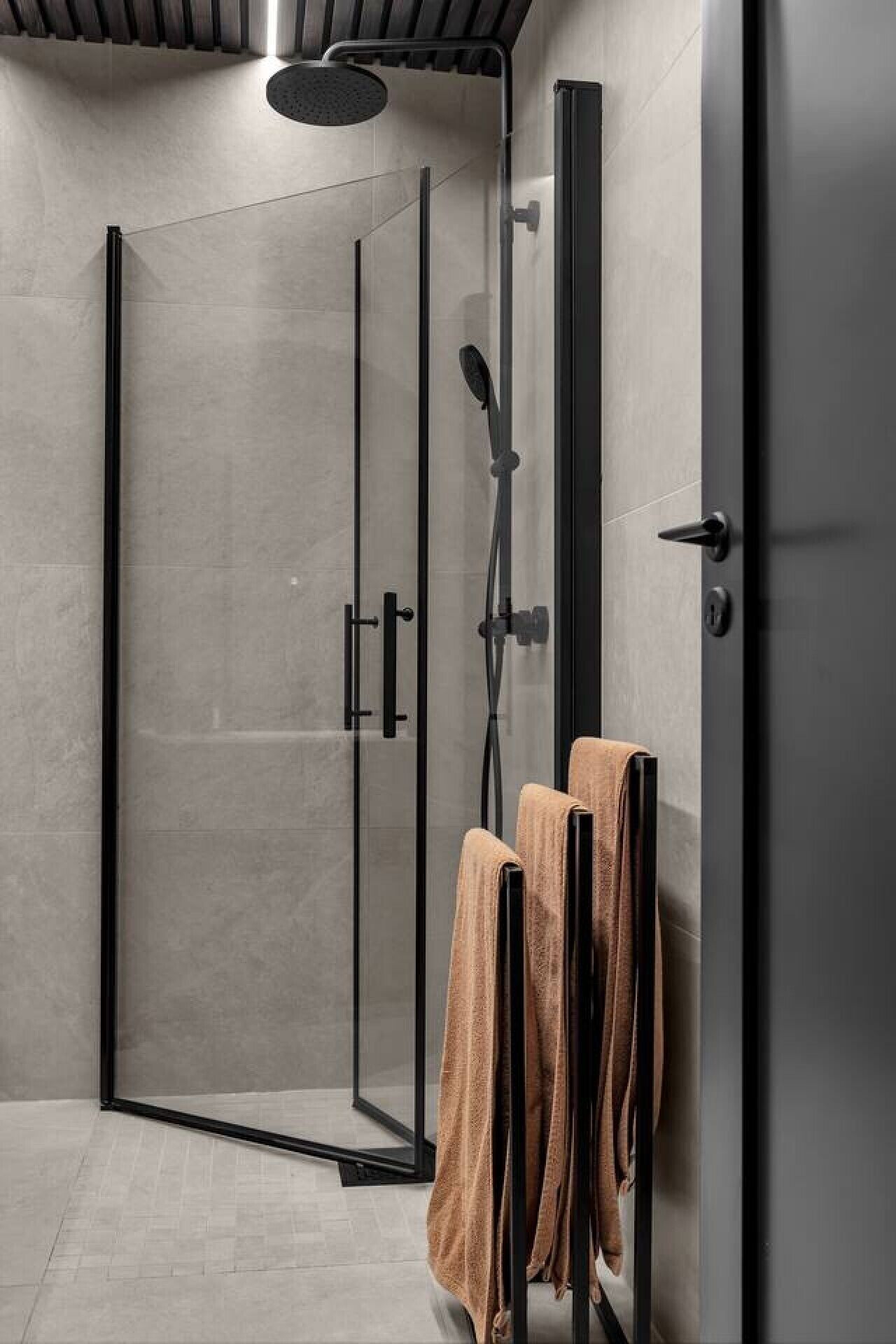 A modern shower enclosure with a glass door, a handheld showerhead, and a towel rack with towels.