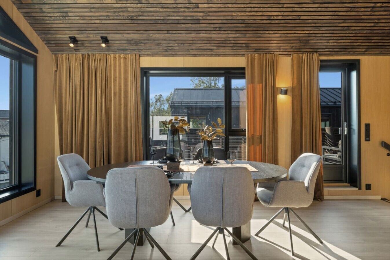 A modern dining area with a round table, four chairs, and a vase with flowers.
