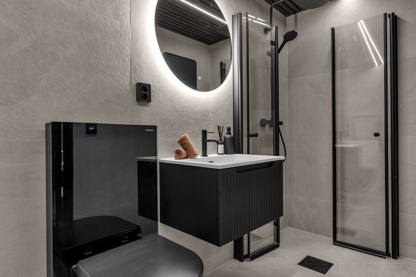 Une salle de bain moderne dotée de toilettes intégrées, d’un meuble-lavabo avec miroir, d’une cabine de douche et d’une porte de douche en verre.