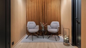 Een kleine, afgesloten ruimte met twee grijze stoelen, een tafeltje met een vaas en een vloerlamp.