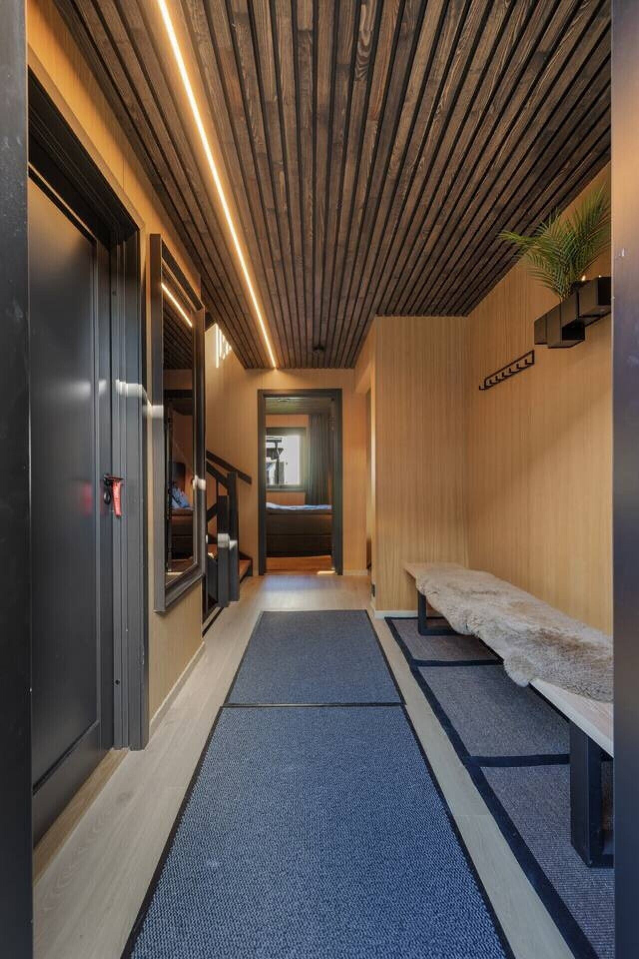 Un couloir avec un plafond en bois, un banc et une porte donnant sur une pièce.