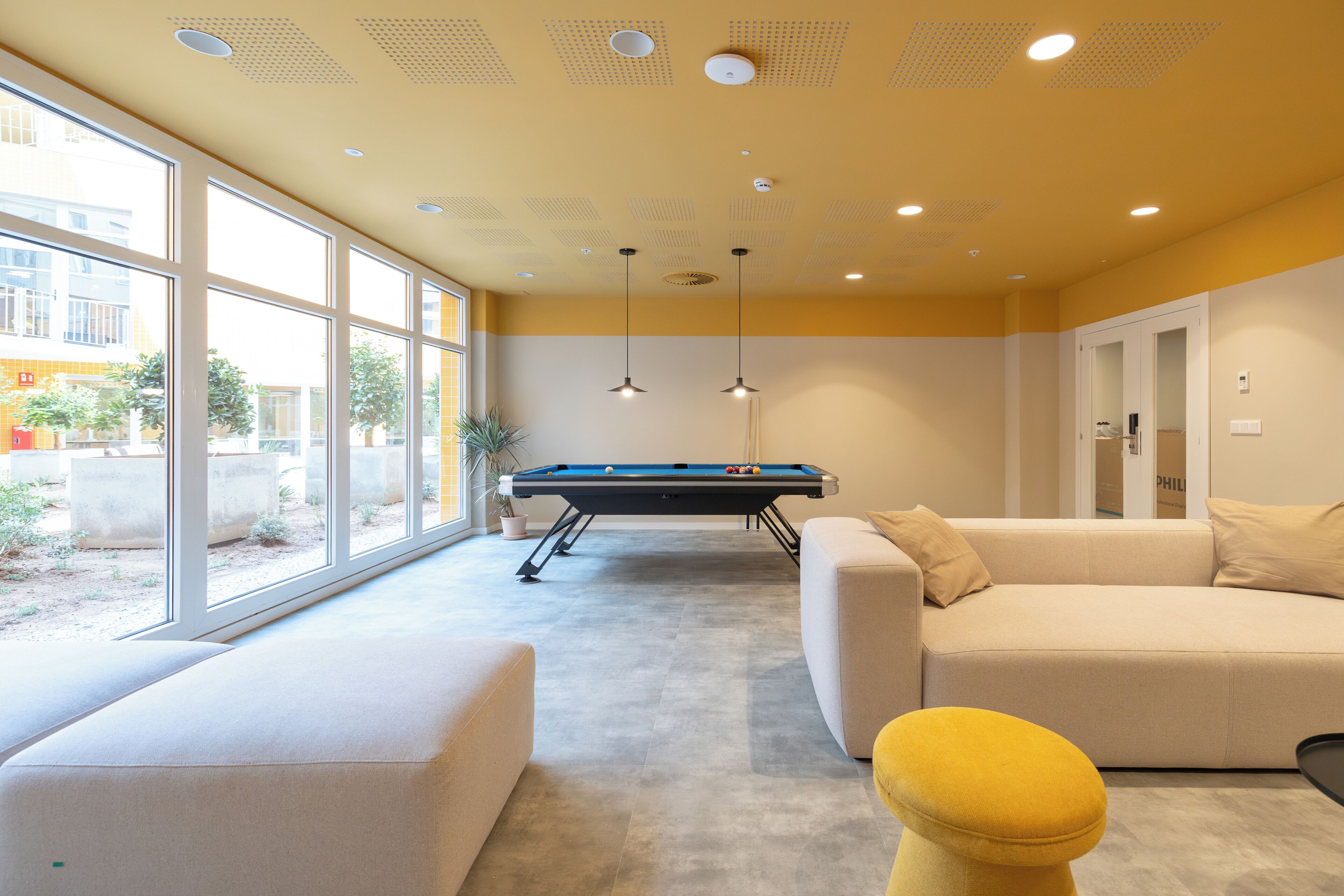A pool table in a room with large windows, a sofa, and a yellow ottoman.