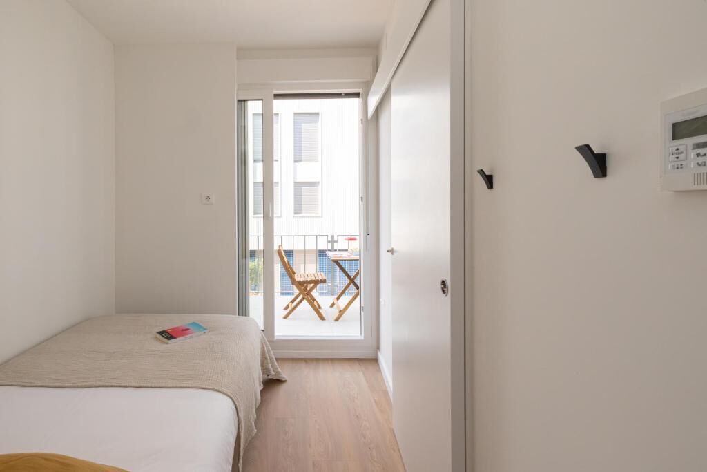 A bedroom with a bed, a bedside table, a chair, and a view of an outdoor balcony.