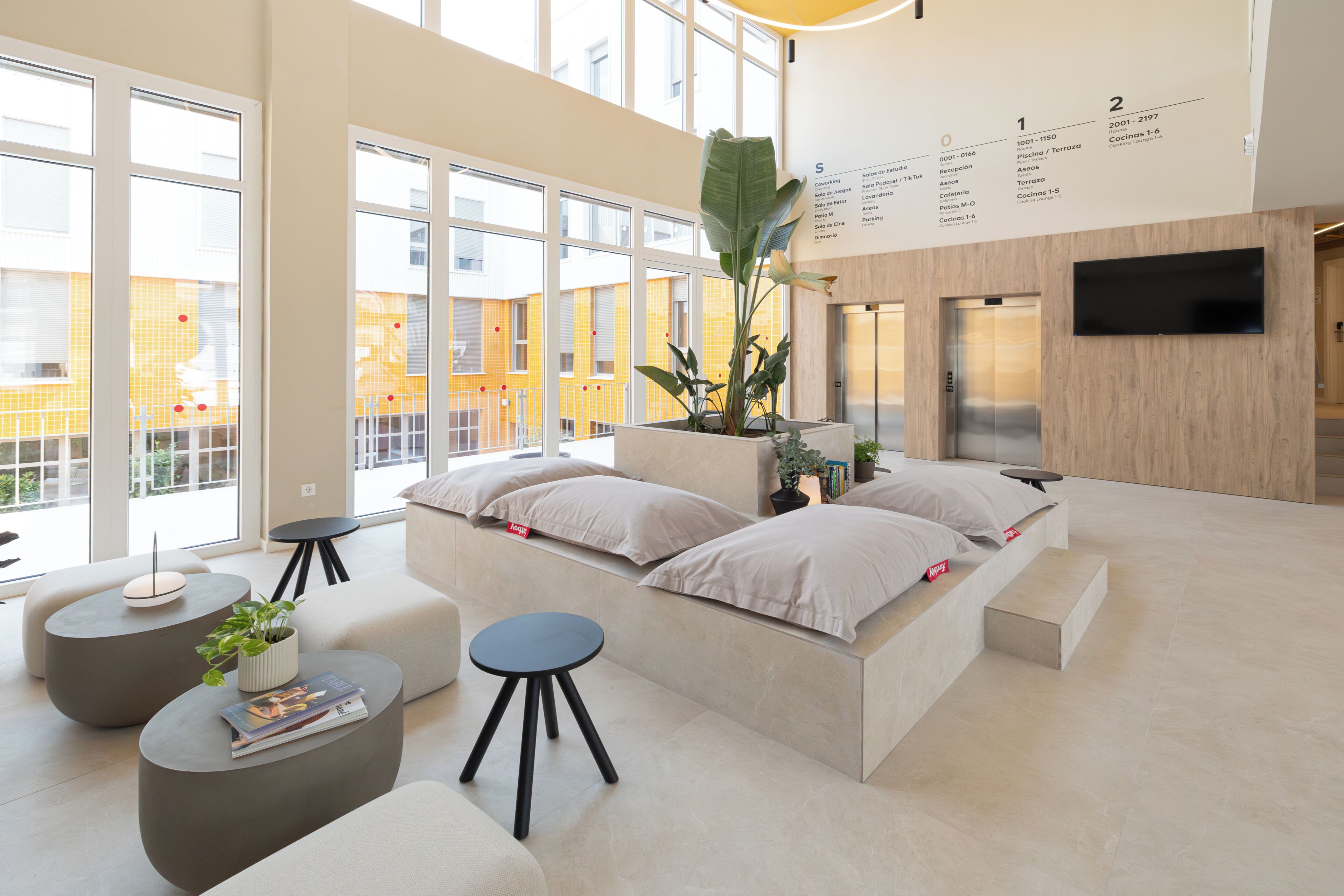 A modern hotel lobby with a seating area, a reception desk, and a large window offering a view of the city.