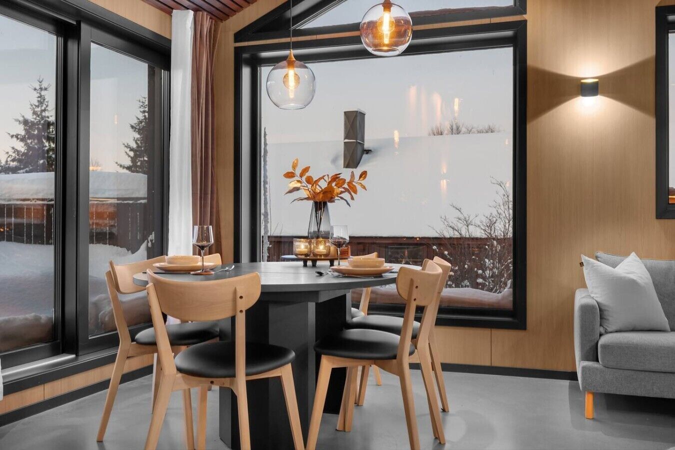 A modern dining area with a round table, wooden chairs, and a vase with autumn leaves.
