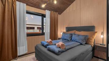 A bedroom with a large bed, wooden ceiling, and a window with curtains.