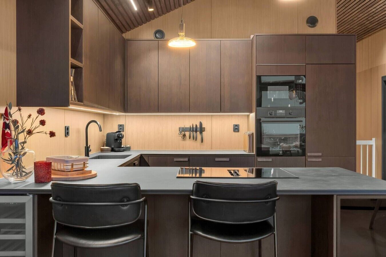 Una cocina moderna con armarios de madera oscura, una isla grande con taburetes de bar y electrodomésticos integrados.