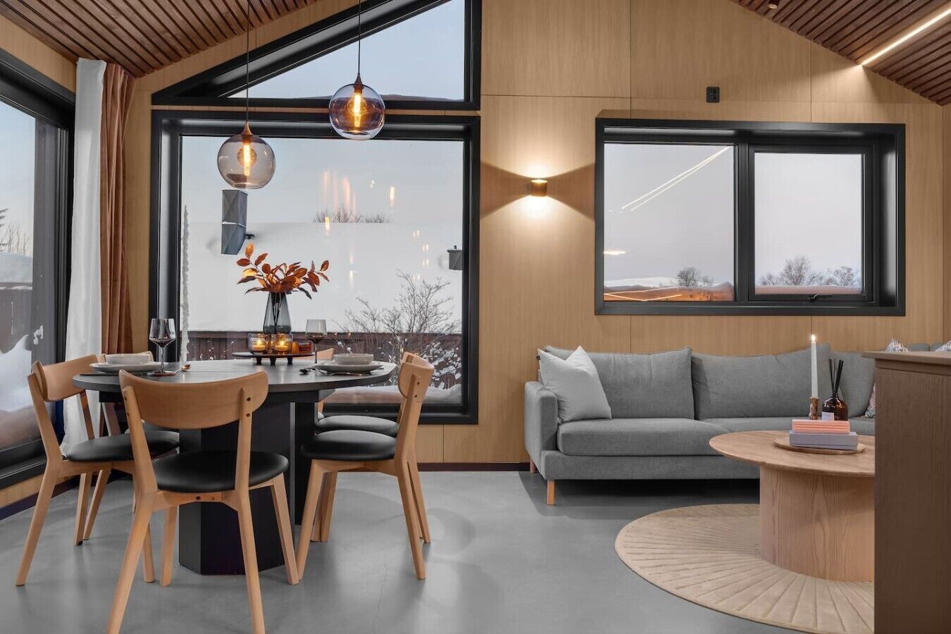 A modern interior with a dining area, a sofa, and a view through large windows.