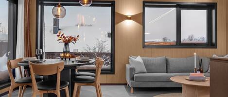 A modern interior with a dining area, a sofa, and a view through large windows.