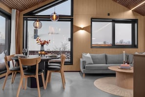 A modern interior with a dining area, a sofa, and a view through large windows. - Signature Townhouse | Arctic Seasons|Luxury Living (Tromsø)