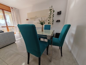 Un comedor con sillas color turquesa, una mesa de vidrio y un florero con flores.