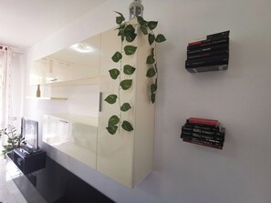 Moderni huone, jossa on suuri kaappi, pieni kasvi ja seinällä pinottu kirjakasa.