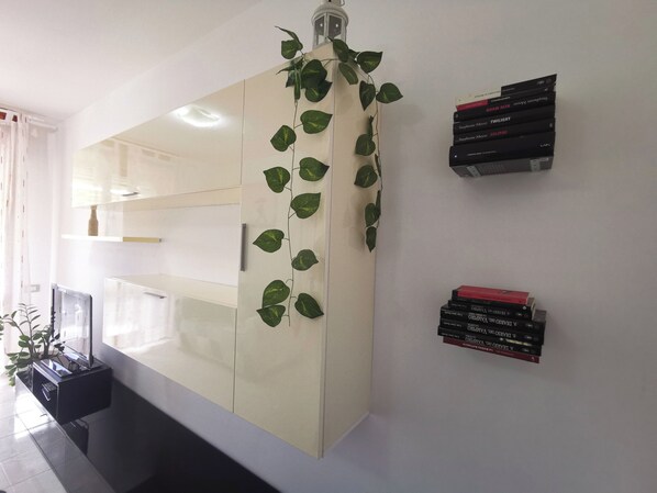 Una habitación moderna con un mueble grande, una planta pequeña y una pila de libros en la pared.