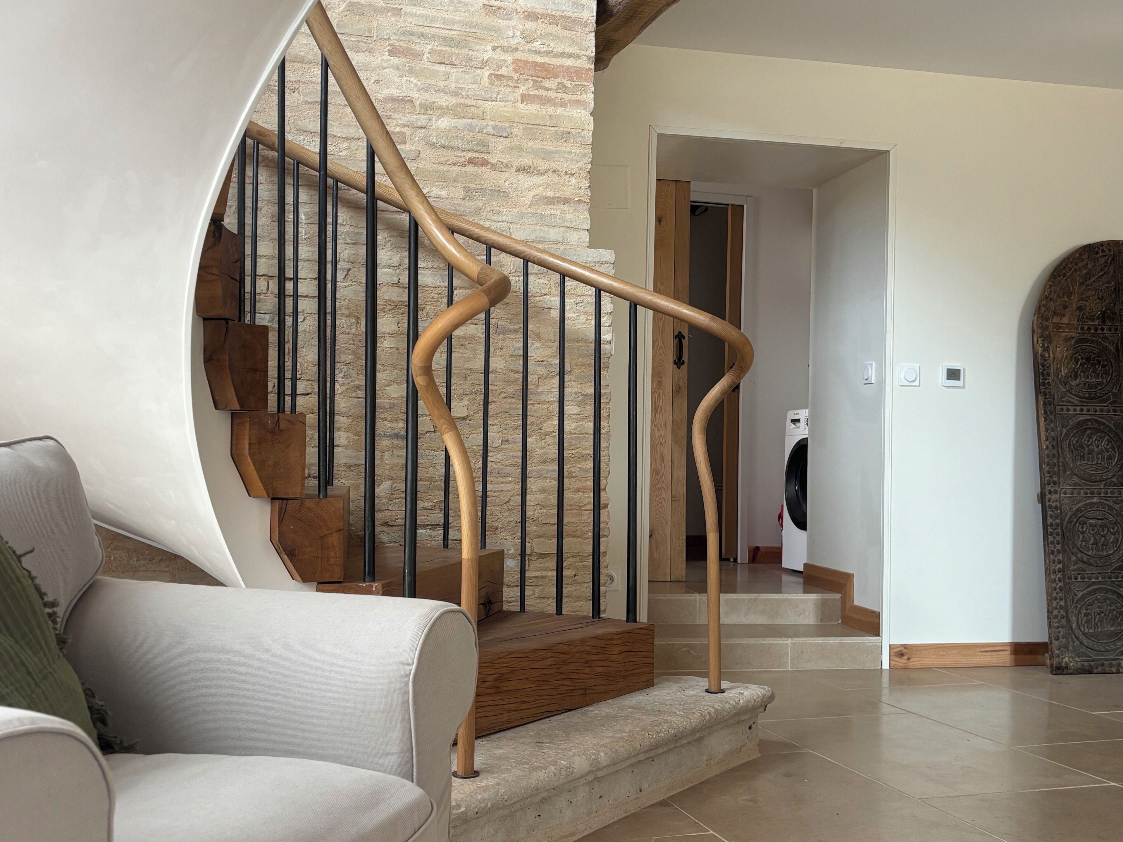 A staircase with a wooden handrail and metal balusters, leading to a room with a washing machine.