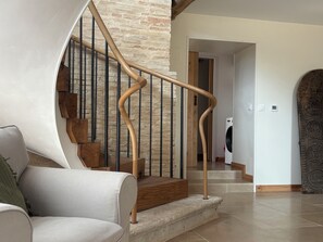 Un escalier avec une main courante en bois et des balustrades en métal, menant à une pièce où se trouve un lave-linge.