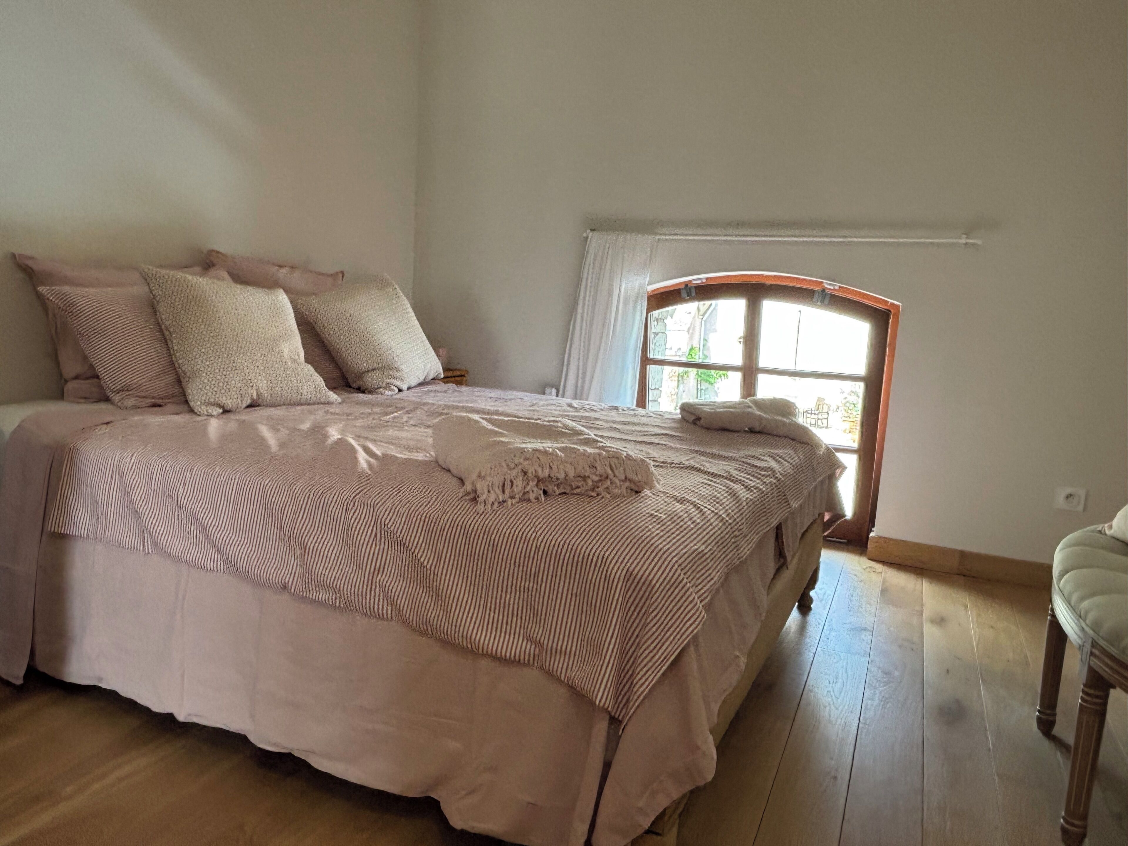 A bedroom with a large bed, a window, and a chair.