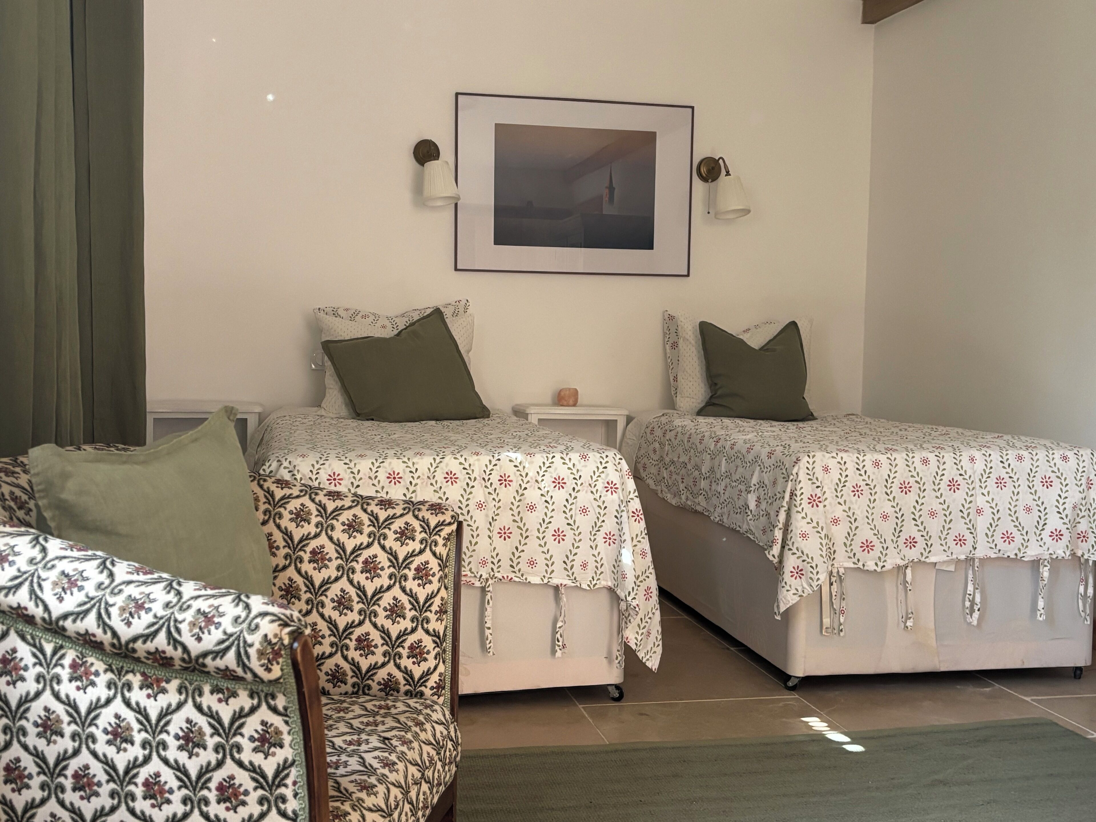 A bedroom with two beds, a nightstand, a lamp, and a framed picture on the wall.