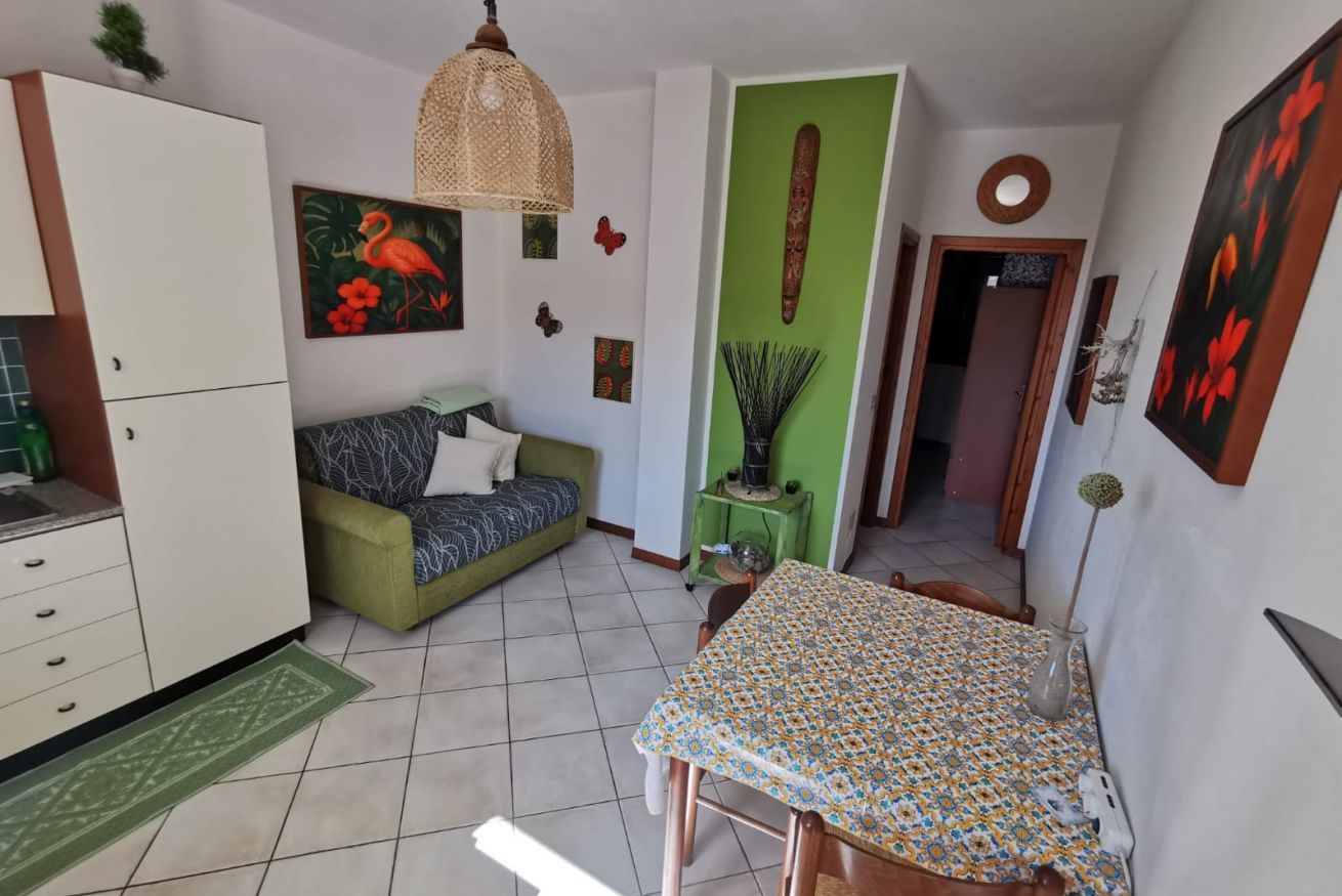 A compact living space with a dining table, sofa, kitchenette, and a green accent wall.
