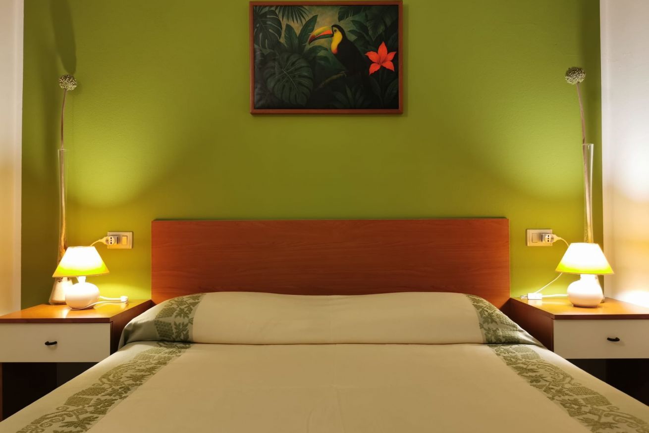 A hotel room with a bed, nightstands, lamps, and a painting on the wall.