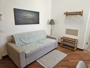 Een woonkamer met een bank, een vloerkleed, een lamp, een kapstok en een schilderij aan de muur.