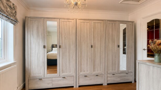 A room with a large wardrobe, a chandelier, and a window with curtains. - Spacious 4BDR Home in Rayleigh Essex (Essex)