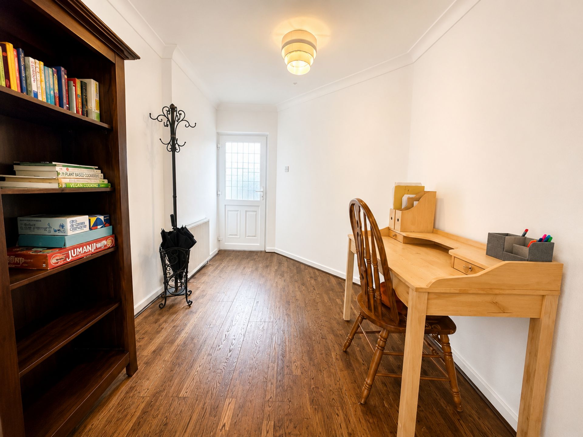 A room with a wooden desk, a chair, a bookshelf with books, and a coat stand.