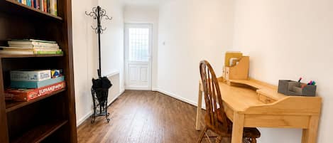 Una habitación con un escritorio de madera, una silla, una estantería llena de libros y un perchero.