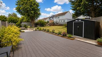 A residential backyard with a wooden deck, a shed, and a lawn.