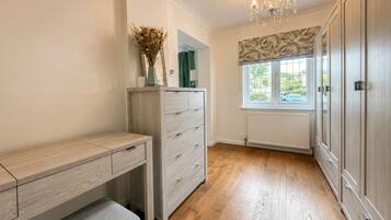 A room with a wooden desk, a bench, a dresser, a radiator, and a window with a view.