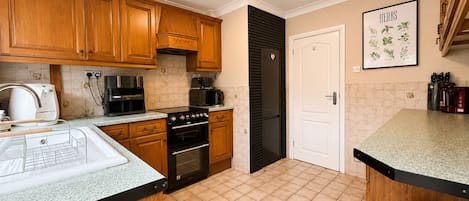 Una cocina moderna con armarios de madera, un refrigerador negro, una cafetera y piso de baldosas.