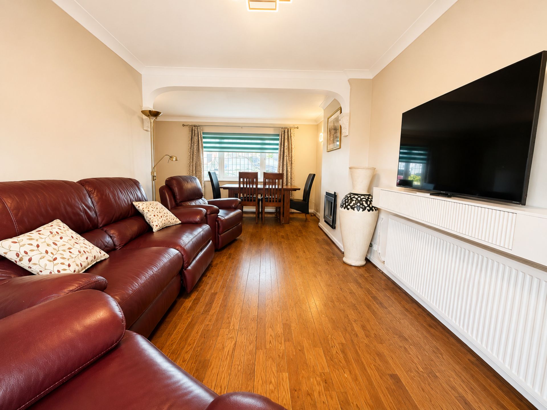 A living room with a sofa set, a dining table with chairs, a television, and a radiator.