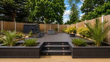 A backyard with a wooden deck, a barbecue area, and a small shed.