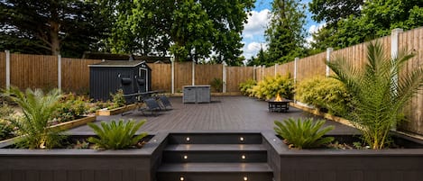 Un patio trasero con terraza de madera, zona de barbacoa y un cobertizo pequeño.