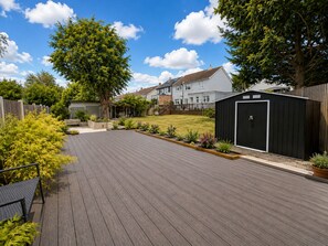 A residential backyard with a wooden deck, a shed, and a lawn.